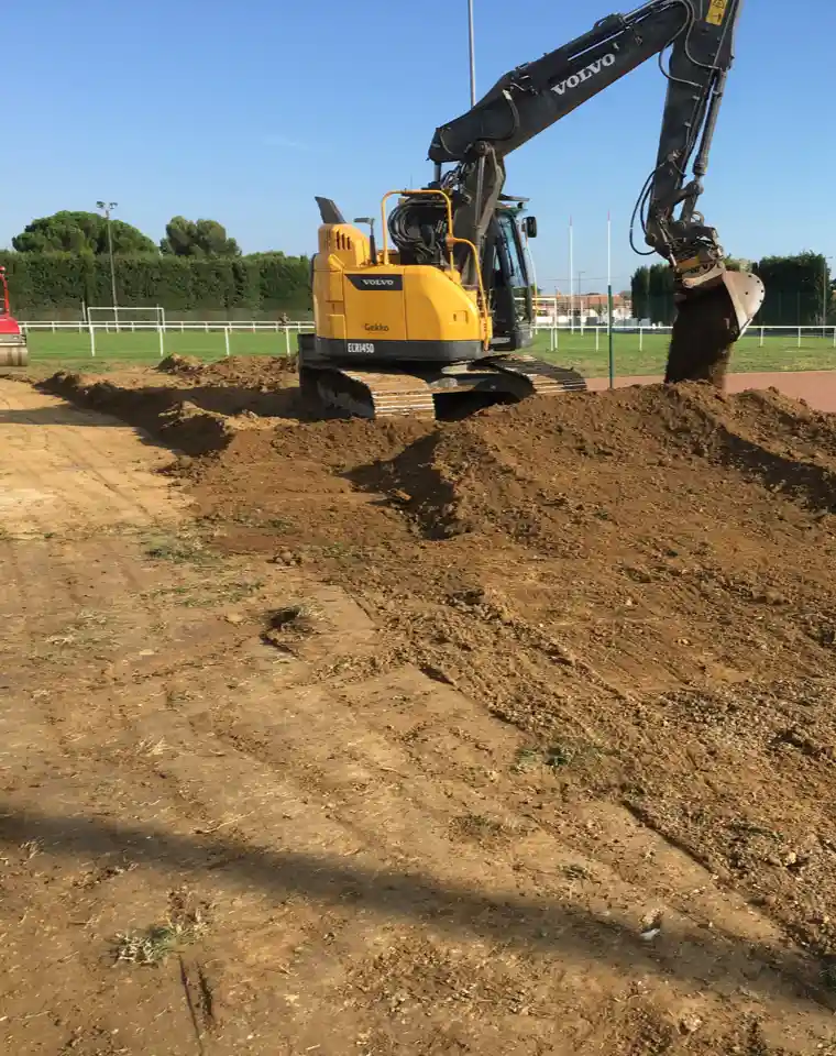 Terrassement d'un terrain de sport avec pelleteuse en action